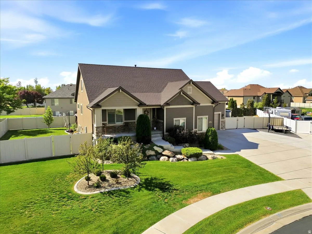 Contemporary residence featuring a paved driveway, a gabled roofline, a fenced backyard, an expansive front lawn, and established landscaping