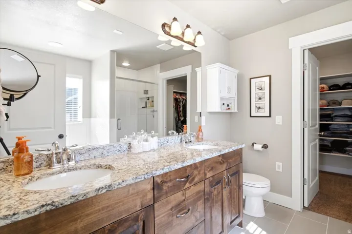 Double vanity with undermount sinks and wood-finish cabinetry, stone countertop, separate water closet, and a glass-enclosed shower