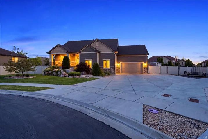 Stone accent siding, covered front porch, attached garage, concrete driveway, and front yard landscaping