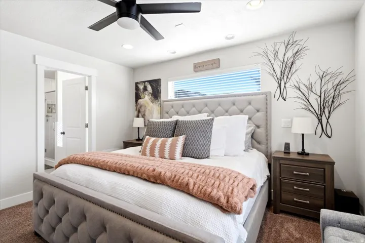 Primary Bedroom featuring a tufted upholstered headboard, recessed ceiling lighting, ceiling fan with integrated light fixture, wood-finish nightstands with drawer storage, and large window with horizontal blinds and transom detailing