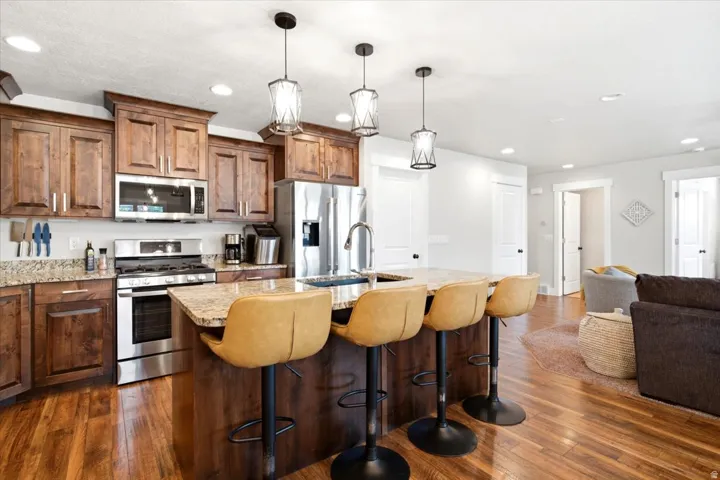 Kitchen featuring wood-finish flooring, stainless steel appliances, pendant lighting, and a kitchen island with seating