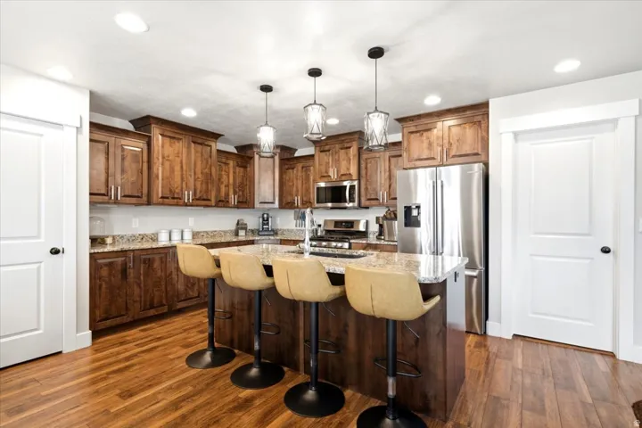 Expansive kitchen with wood-finish flooring, custom wood cabinetry, stainless steel appliances, and a granite-topped island