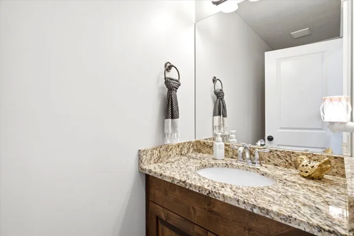 Vanity with a granite countertop, undermount sink, chrome faucet, and wood-finish cabinetry