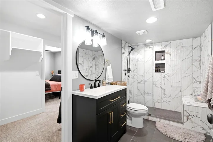 Bathroom featuring a modern black vanity with gold-tone hardware, white countertop, round mirror, and a walk-in shower with tile surround and built-in niches