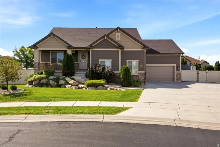 Contemporary exterior with stone accenting, an attached garage, landscaped front yard with rock features, a paved driveway, and perimeter fencing