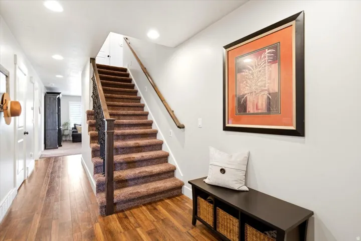 Hardwood-finish flooring, carpeted staircase, wood handrail, and white walls