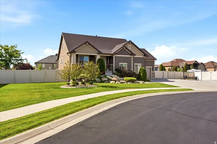 Siding exterior with stone accents, covered front entry, attached garage, manicured lawn, and mature landscaping