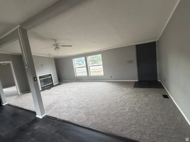 Spacious living area featuring light gray walls, plush carpet, a fireplace, and multiple windows