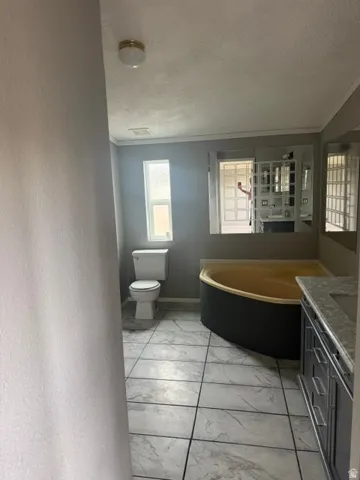 Bathroom featuring a corner soaking tub, single vanity with integrated sink, white tile flooring, and a fixed pane window