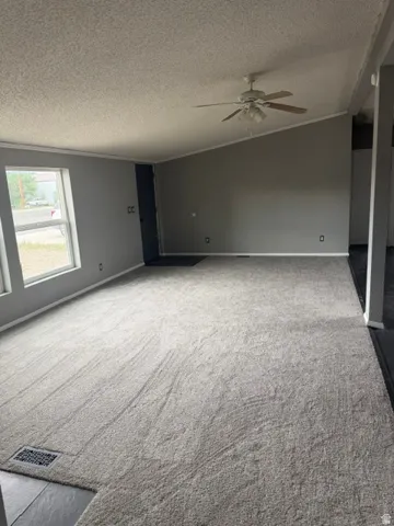 Spacious living area featuring neutral carpeting, light gray wall tones, a ceiling fan, and a vaulted ceiling
