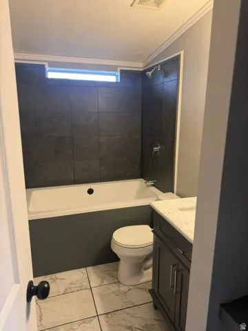 Built-in bathtub with dark tile surround, transom window, white marble-look floor tiles, and a vanity with a white countertop