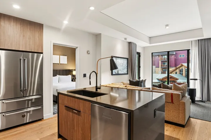 Kitchen with a stainless refrigerator and island sink, open to the living room in this Park City ski-in, ski-out condo.