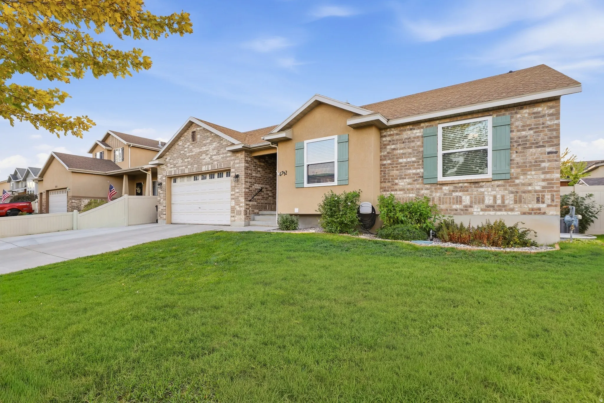 Exterior featuring brick and stucco siding, a concrete driveway, an attached garage, a front lawn, and mature landscaping