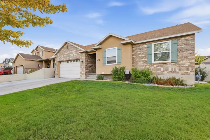 Exterior featuring brick and stucco siding, a concrete driveway, an attached garage, a front lawn, and mature landscaping