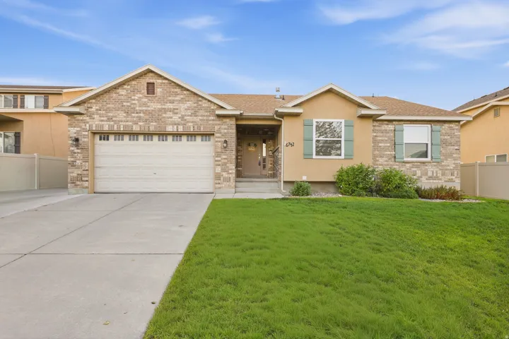 Brick and stucco exterior, attached garage, concrete driveway, front lawn, and foundational plantings