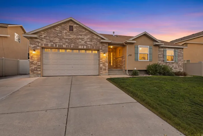 Brick and stucco exterior with stone accents, attached two-car garage, concrete driveway, and front lawn