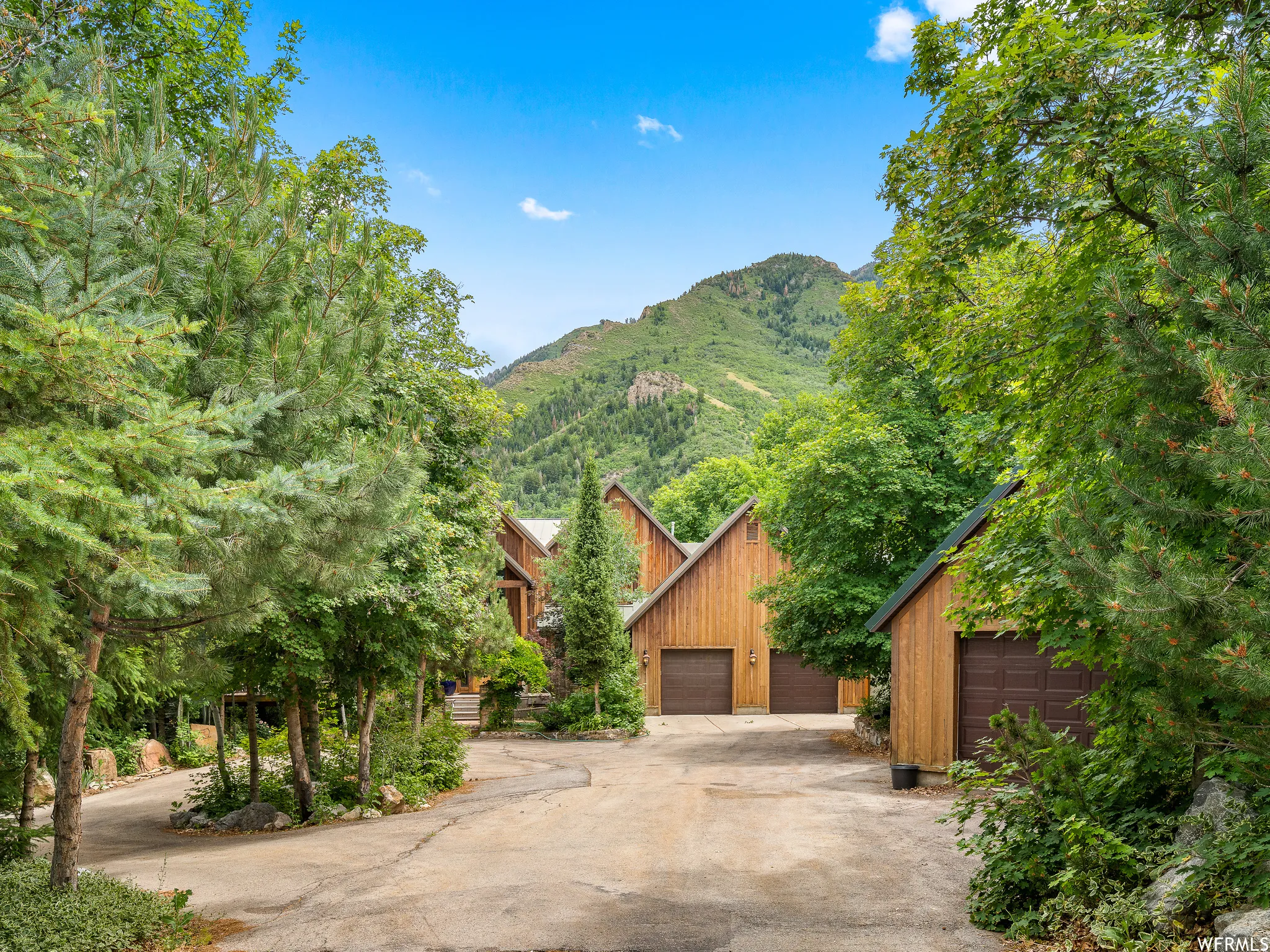 Wood-sided exterior, multiple garage doors, concrete driveway, mature trees, mountainous backdrop