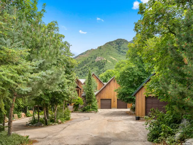 Wood-sided exterior, multiple garage doors, concrete driveway, mature trees, mountainous backdrop