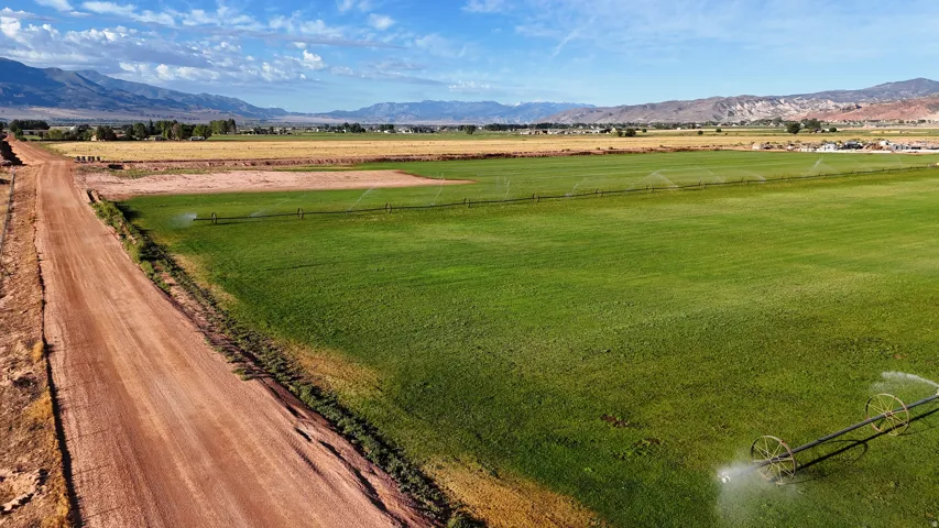 Expansive agricultural land featuring a verdant field, active irrigation system, and a rustic dirt road