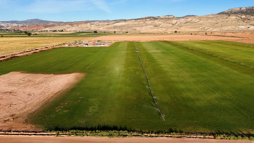 Expansive green fields with irrigation systems, bordered by undeveloped land and distant mountains