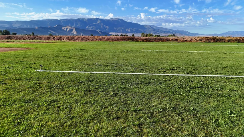 Expansive green field featuring an irrigation system and distant mountain scenery