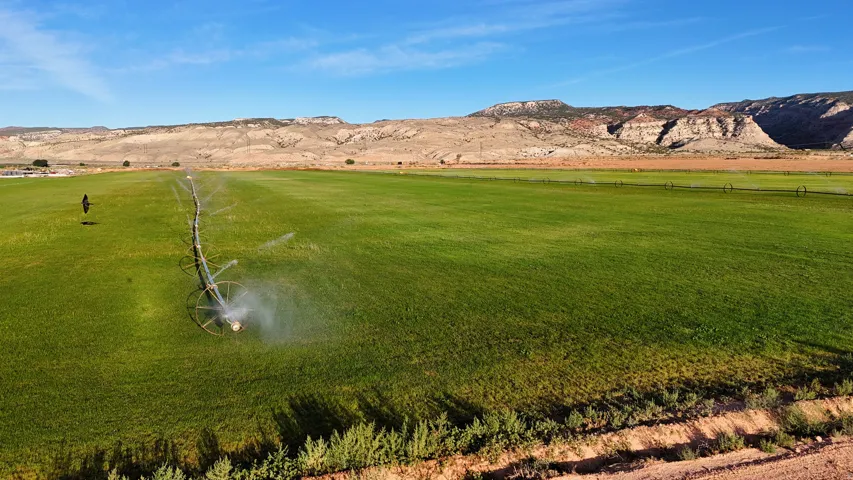 Expansive green field with an irrigation system, bordered by natural land formations