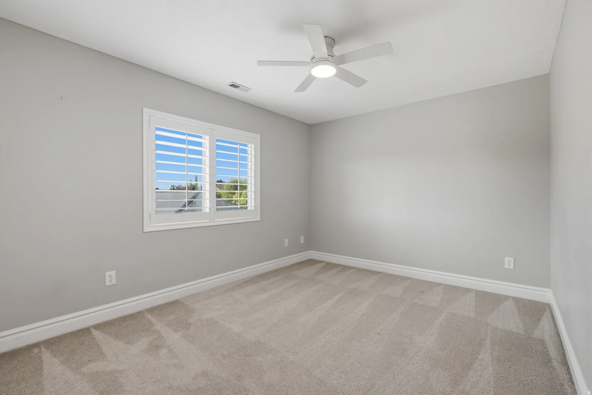 Neutral wall color, carpeted flooring, window with plantation shutters, and a ceiling fan with integrated lighting