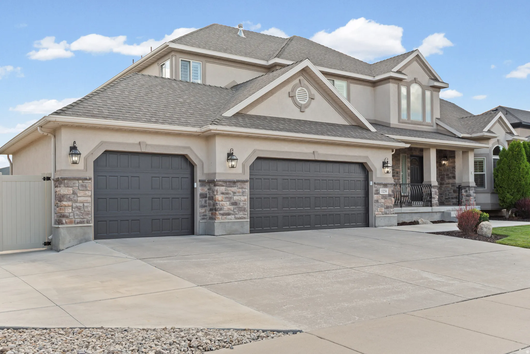 Stucco exterior with stone accents, a multi-car garage, concrete driveway, and front porch with wrought iron railings