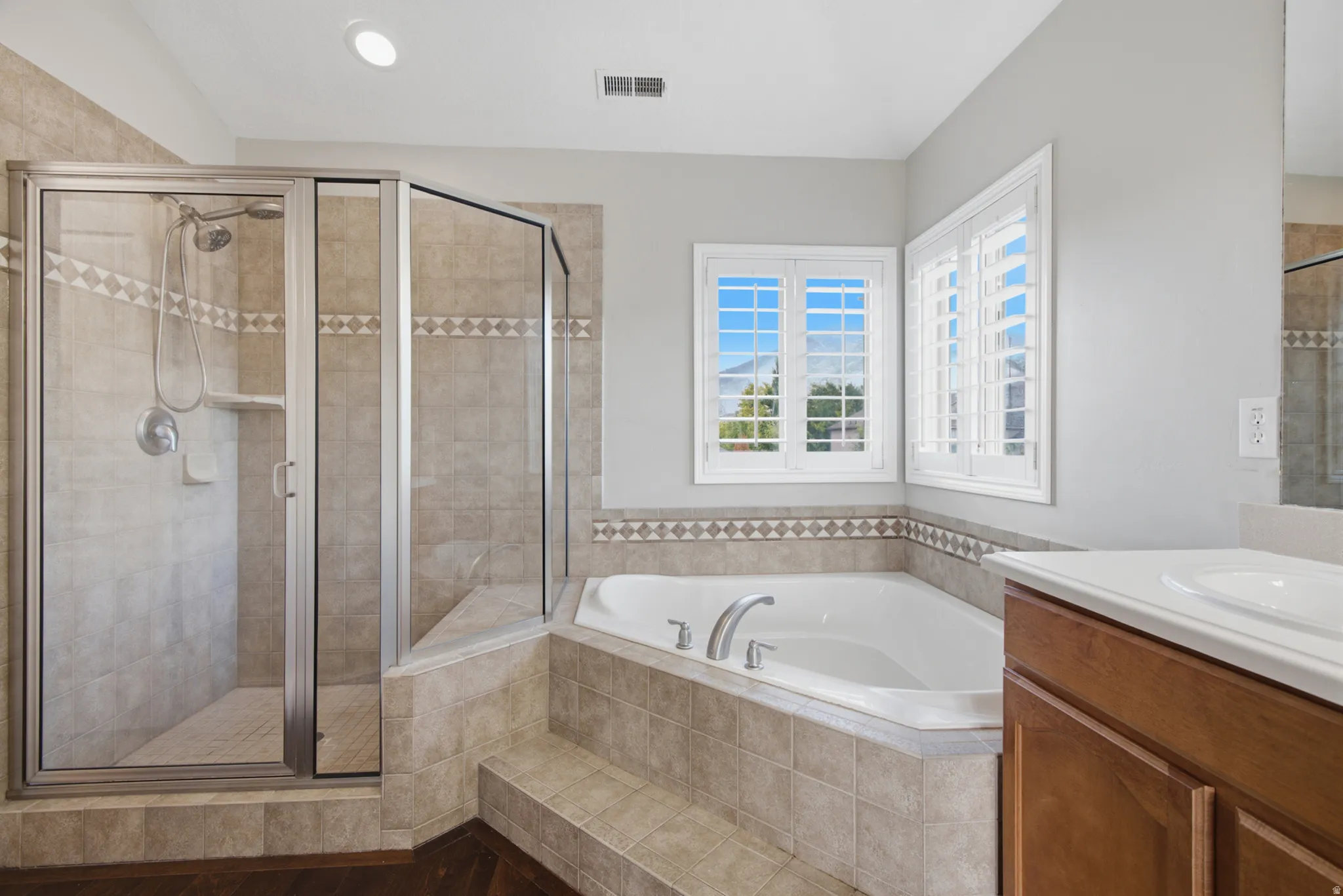 Glass-enclosed shower with a handheld showerhead, corner soaking tub, and white window shutters
