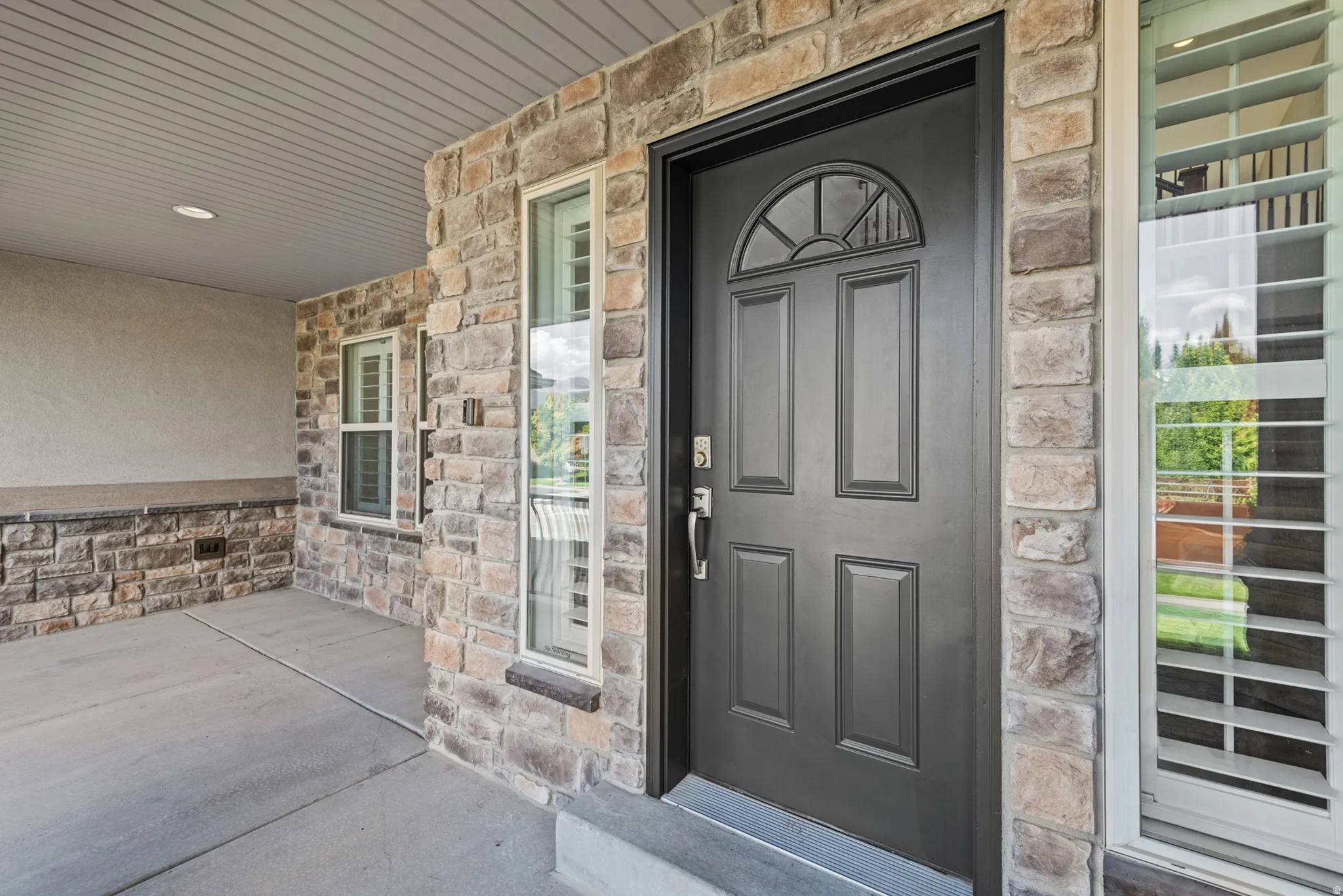 Stone veneer exterior with stucco accents, paneled entry door with transom window, and plantation shutters