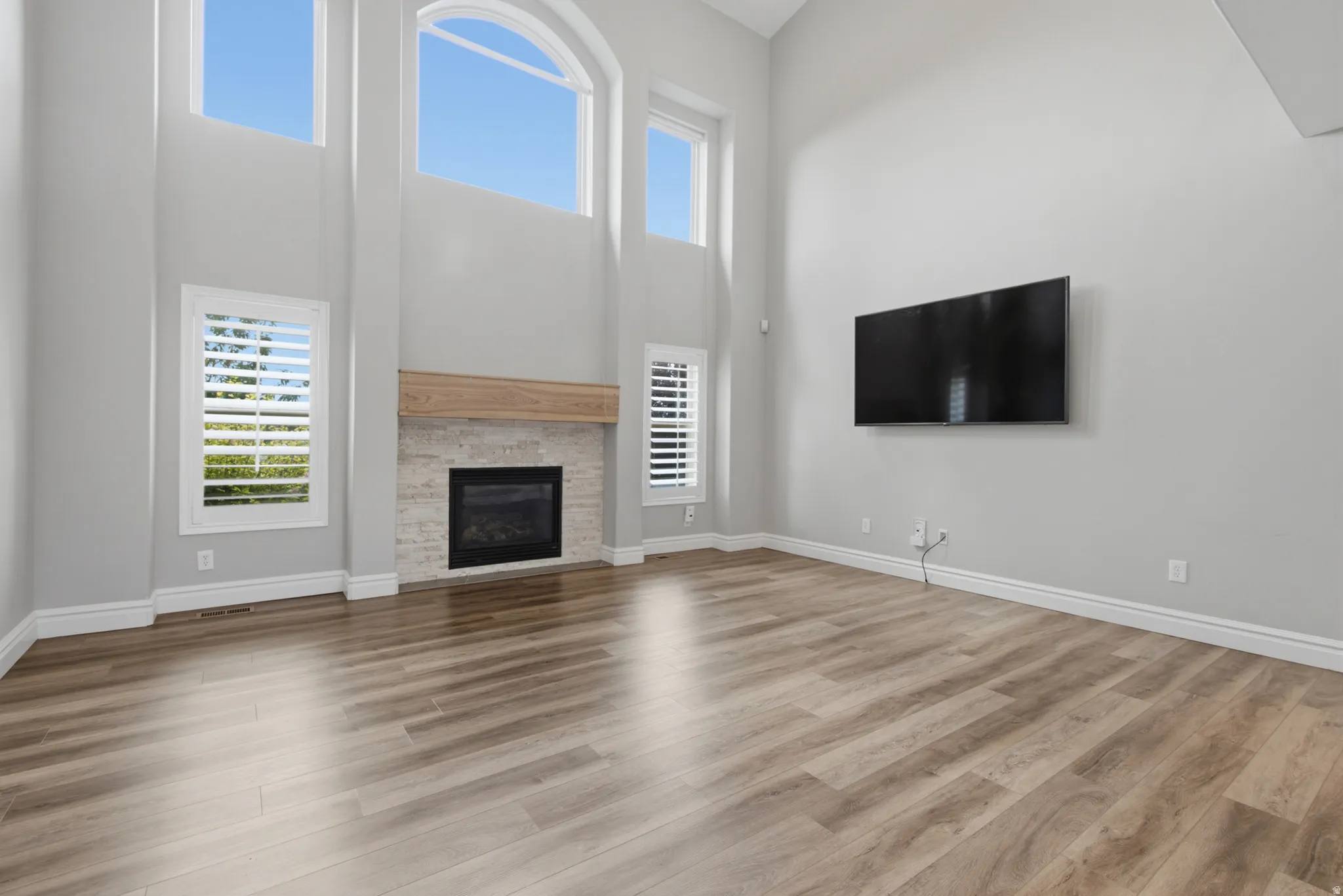 Vaulted ceilings with abundant natural light, a stone-surround fireplace with a wood mantle, custom window shutters, and wood-finish flooring