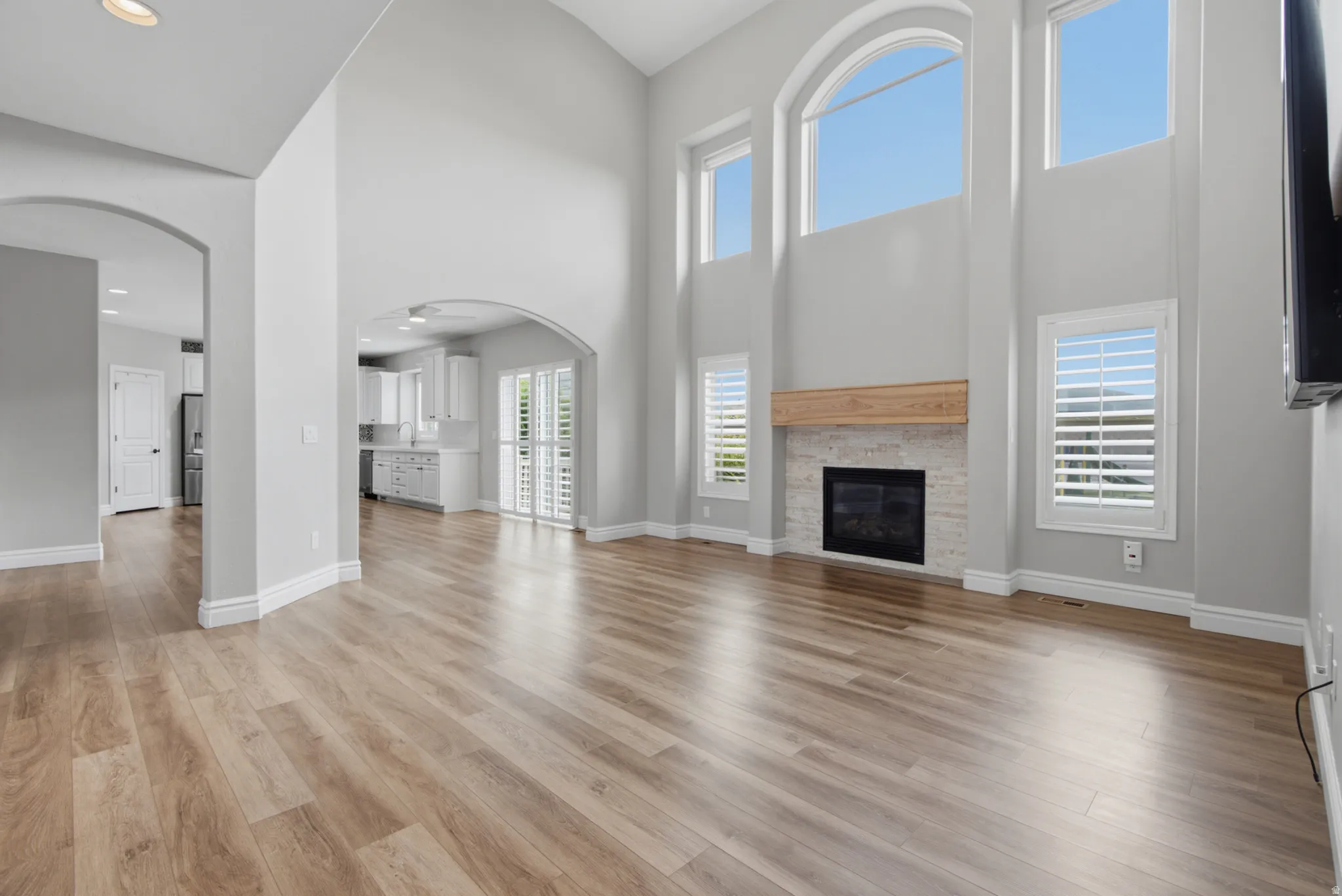 Great room with high ceilings, large arched windows, wood-finish flooring, and a fireplace with a stone surround and wood mantel