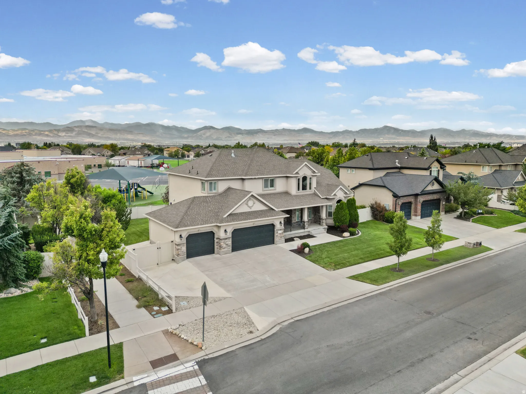Neutral-toned stucco exterior with stone accents, featuring a multi-car garage, mature landscaping, and an expansive concrete driveway