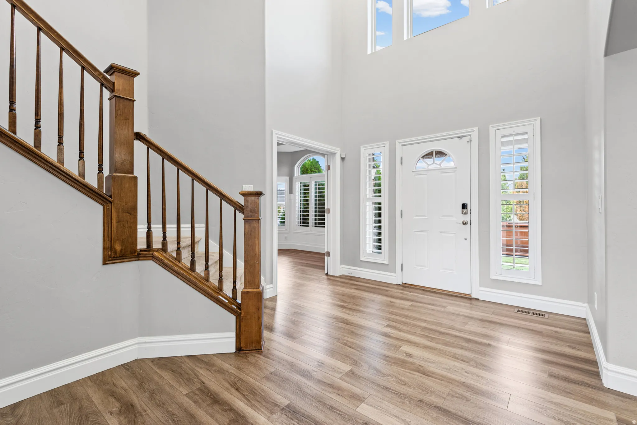 Two-story foyer with wood-finish flooring, a wood staircase, transom windows, and white plantation shutters