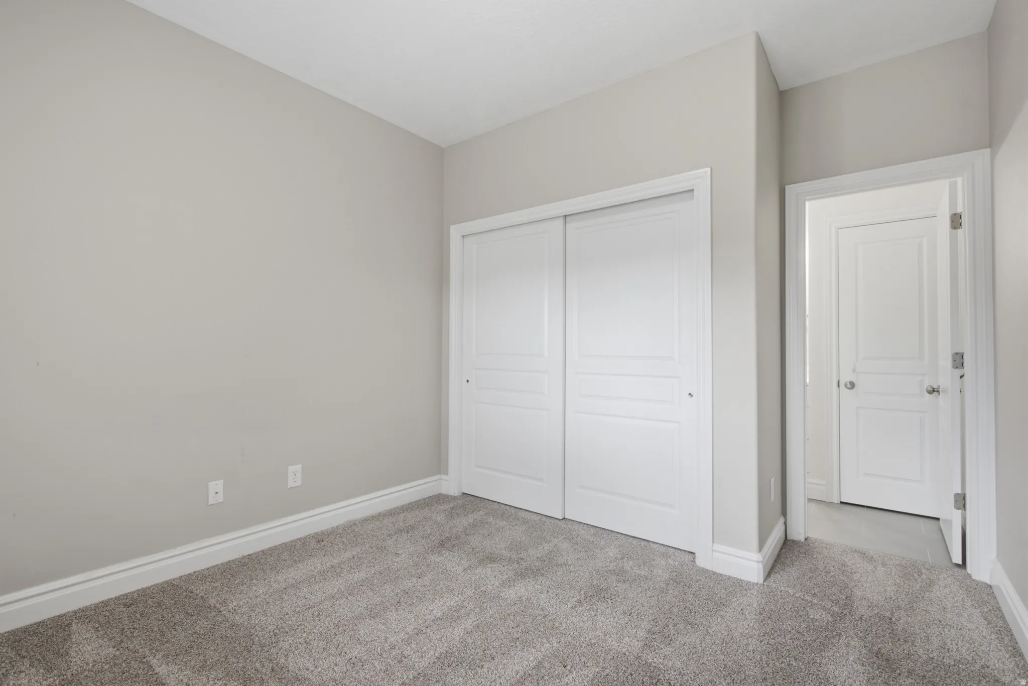 Light gray wall paint, gray carpet flooring, white sliding closet doors, and white interior doors