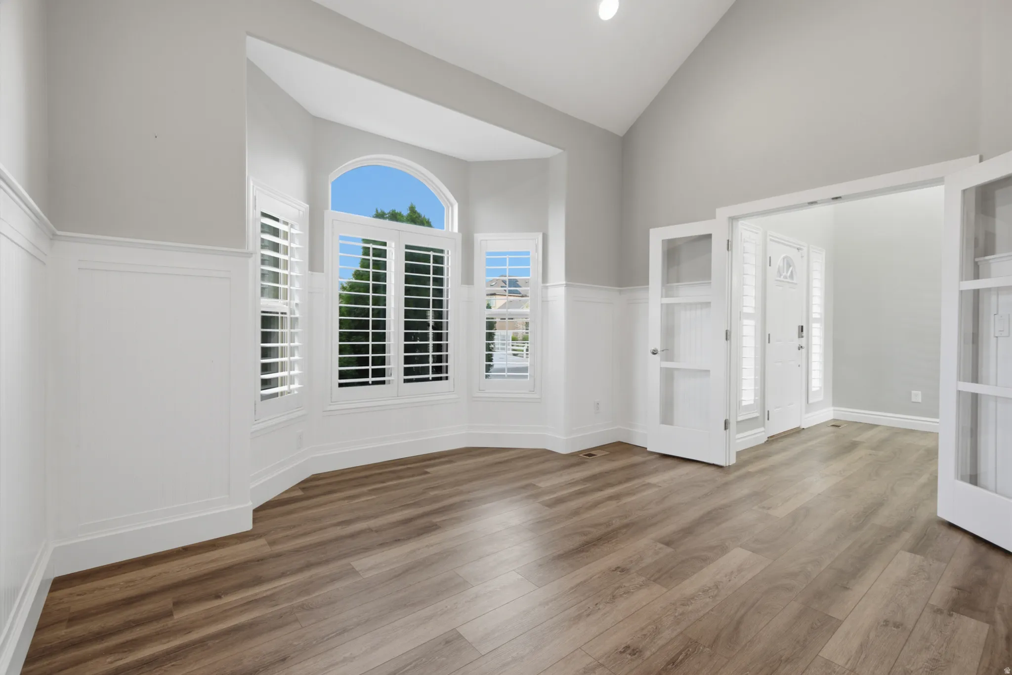 Vaulted ceiling, wood-finish flooring, wainscoting, bay window with shutters, and French doors