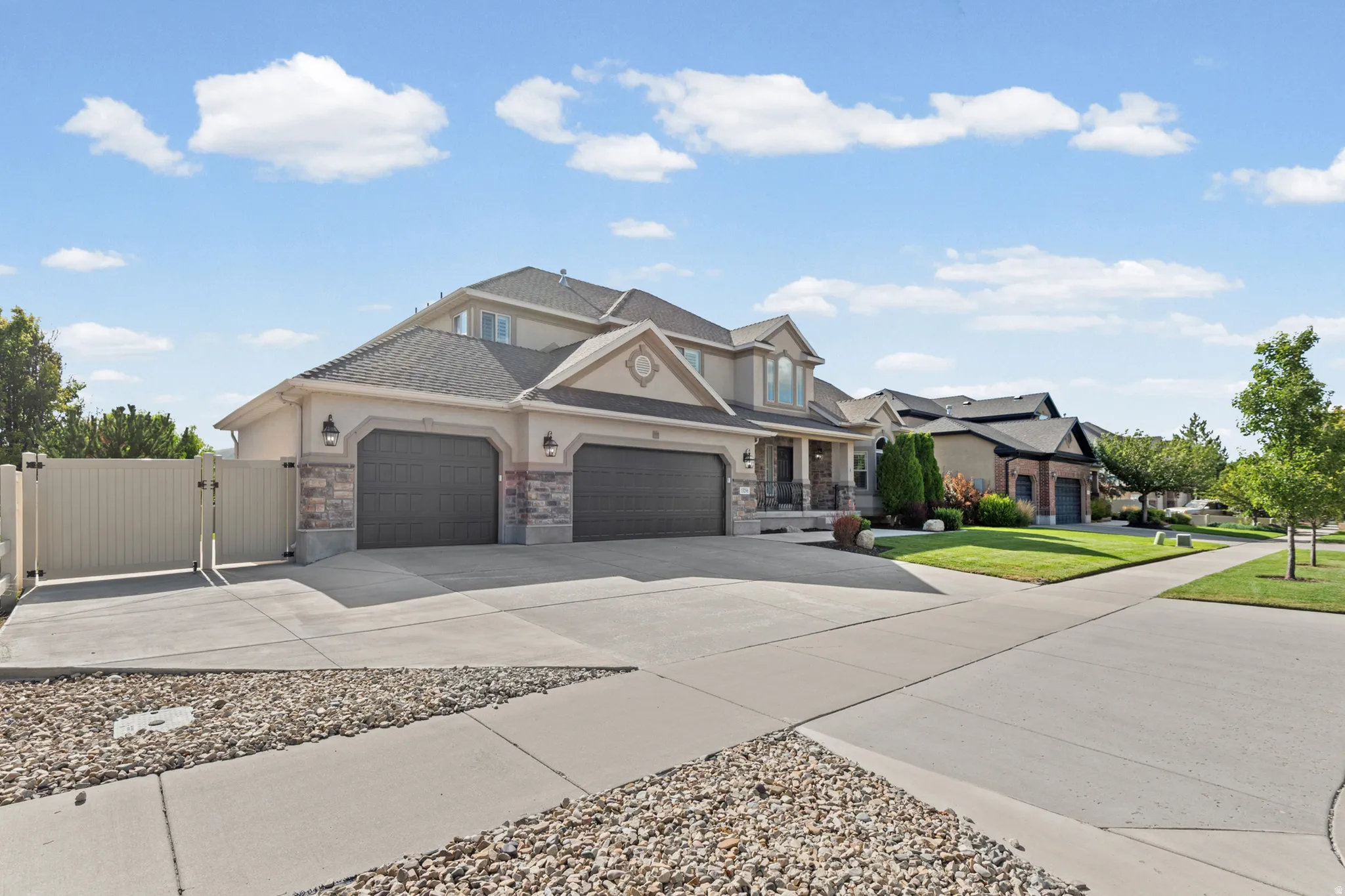 Two-story stucco and stone exterior featuring a multi-car garage, extensive concrete driveway, and a fenced side yard with gate access