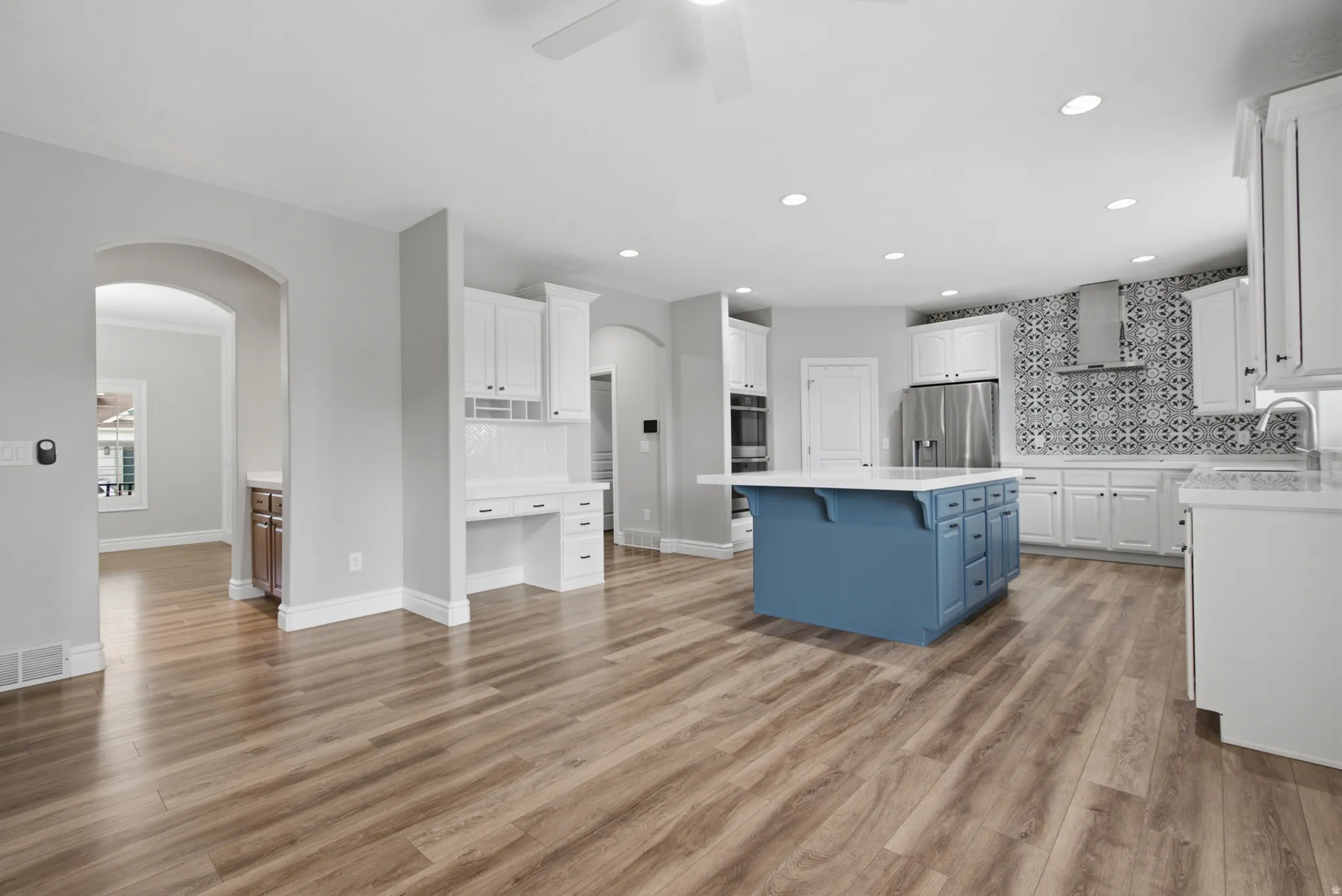 Spacious kitchen featuring an expansive island, stainless steel appliances, a decorative tile backsplash, and white cabinetry