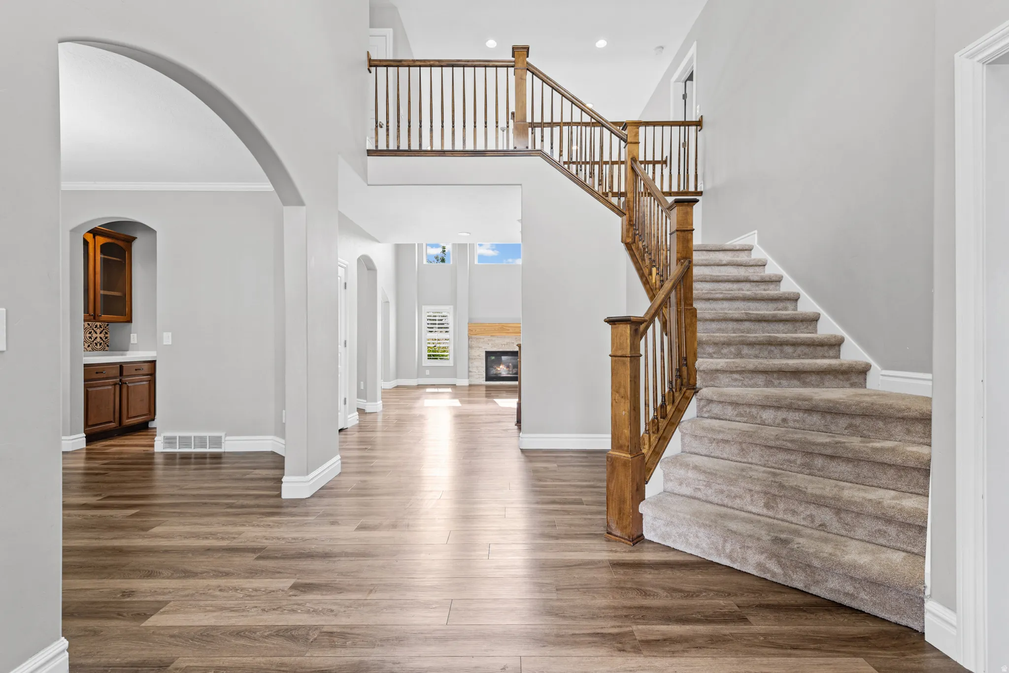 Two-story entryway with wood-finish flooring, a carpeted staircase with wood railing, and an arched doorway leading to built-in cabinetry