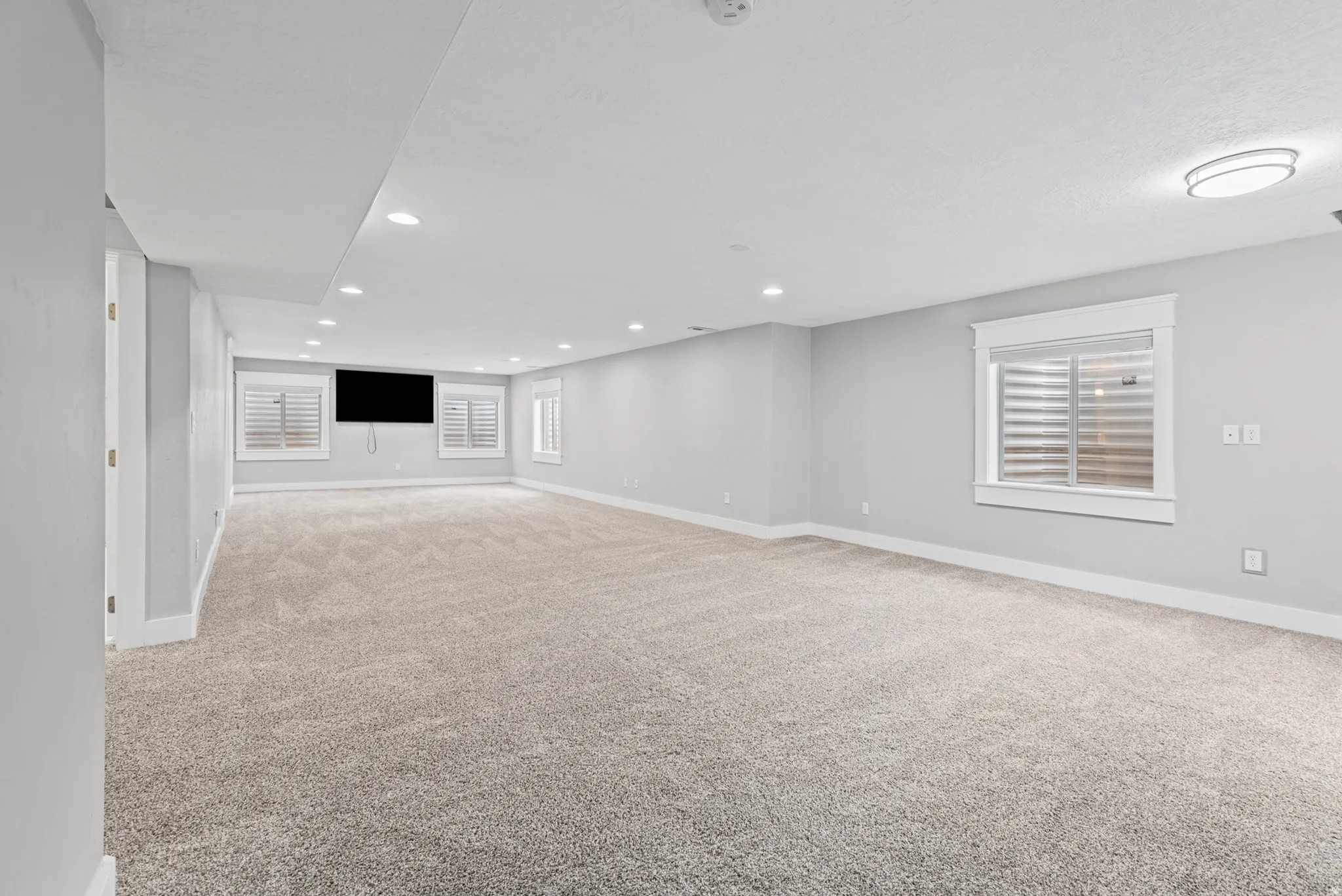 Spacious room with plush carpeting, recessed lighting, and multiple windows with plantation shutters
