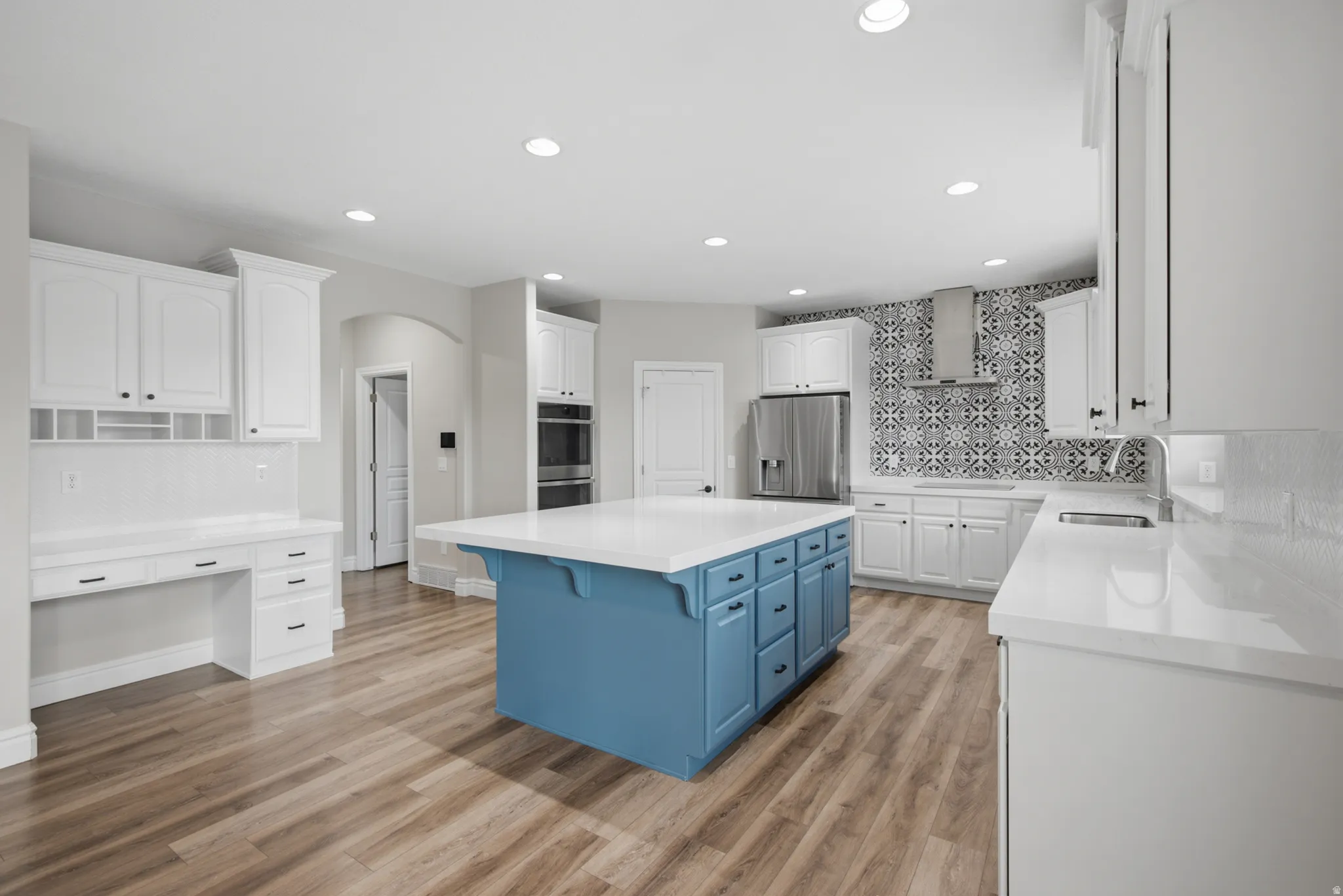 Kitchen featuring a blue-finished island with a white countertop, wood-finish flooring, white cabinetry, stainless steel appliances, and a decorative tile backsplash