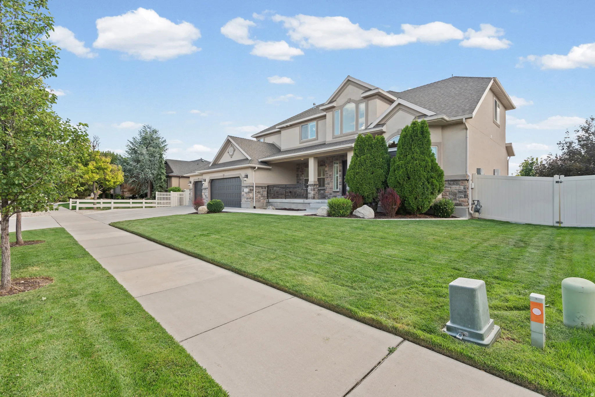 Stucco and stone exterior with a covered porch, attached two-car garage, and established landscaping
