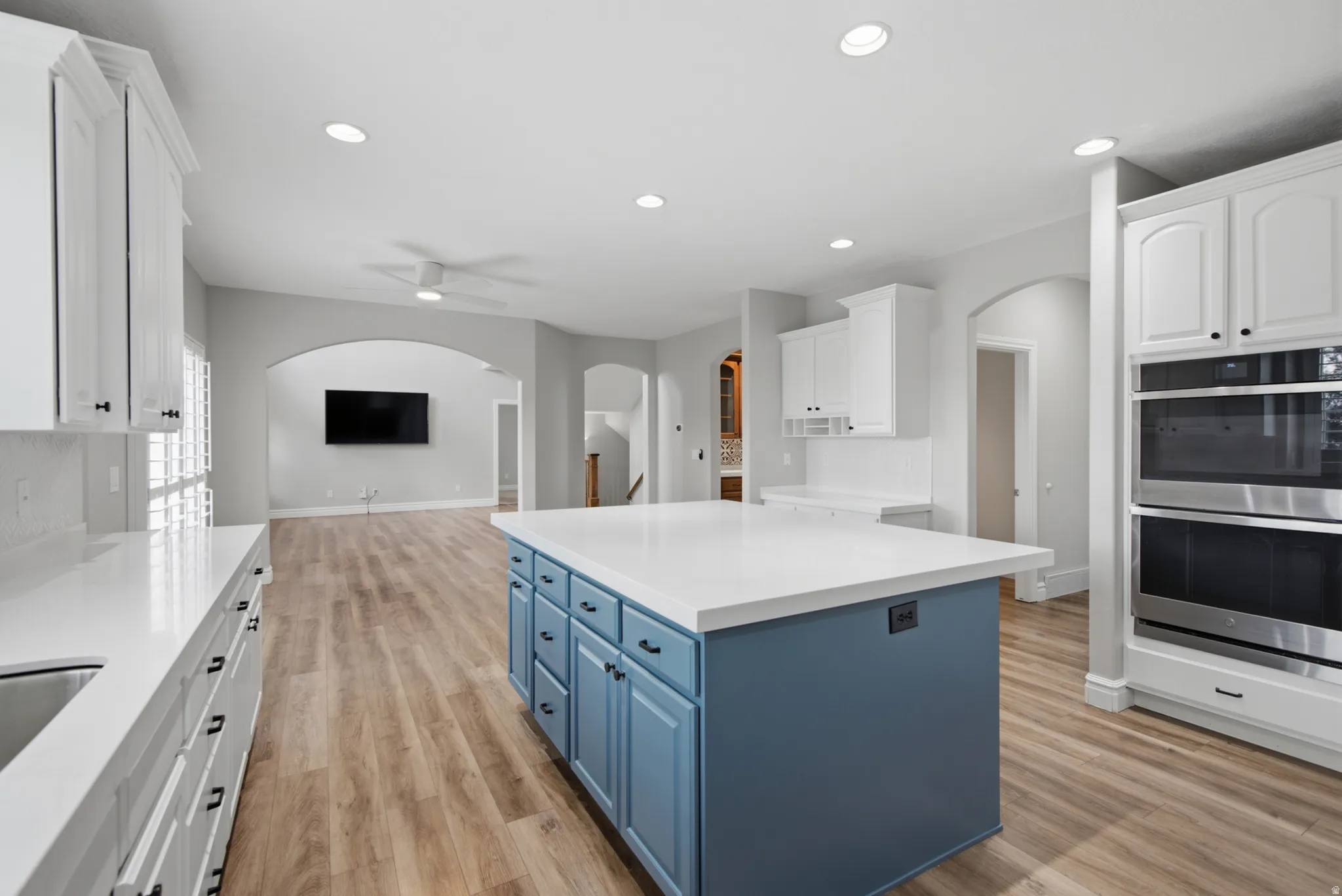 Kitchen featuring a spacious island with a light-toned countertop, white cabinetry, integrated stainless steel double ovens, and wood-finish flooring