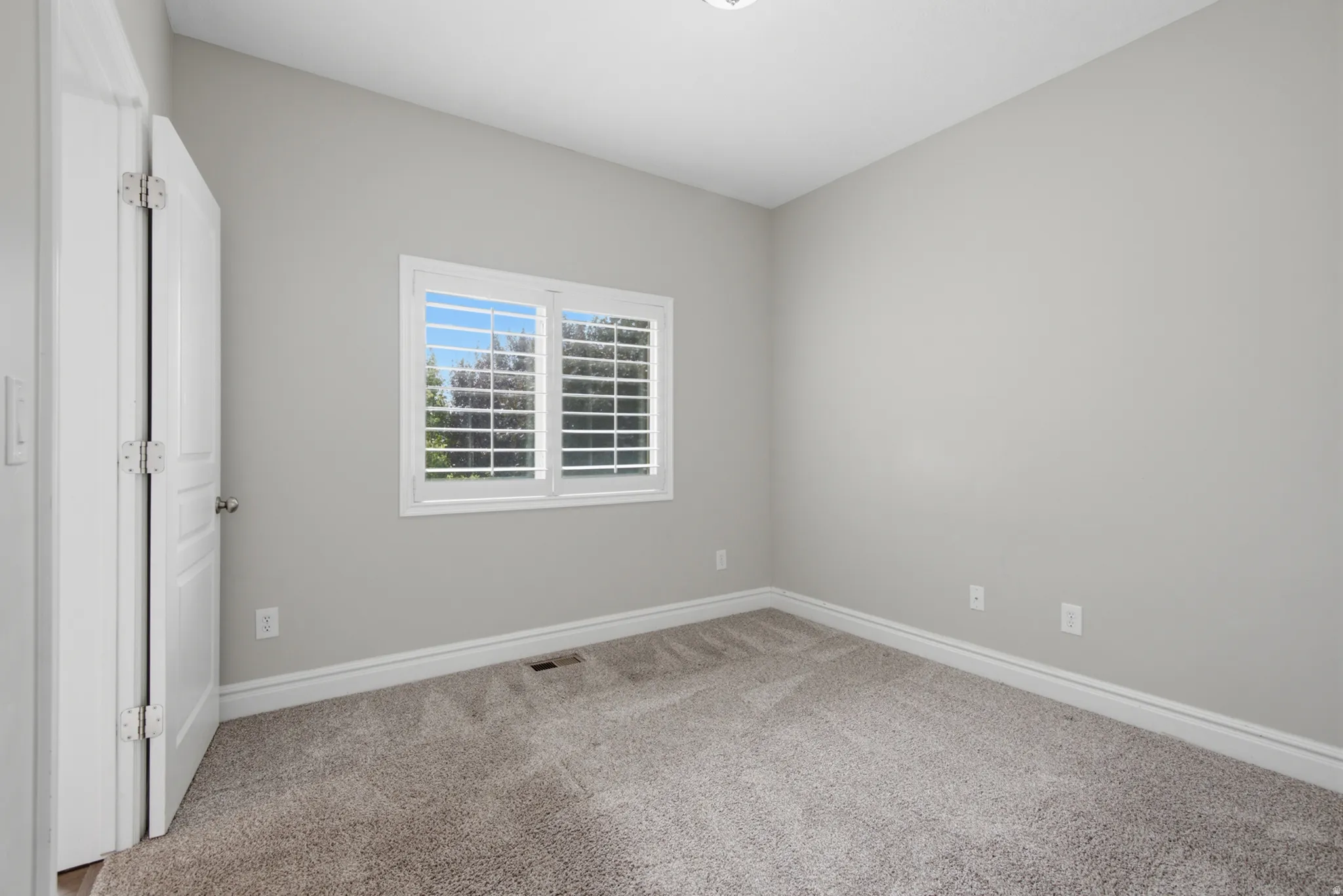 Neutral wall paint, carpeted flooring, window with plantation shutters, white trim, and a white paneled door