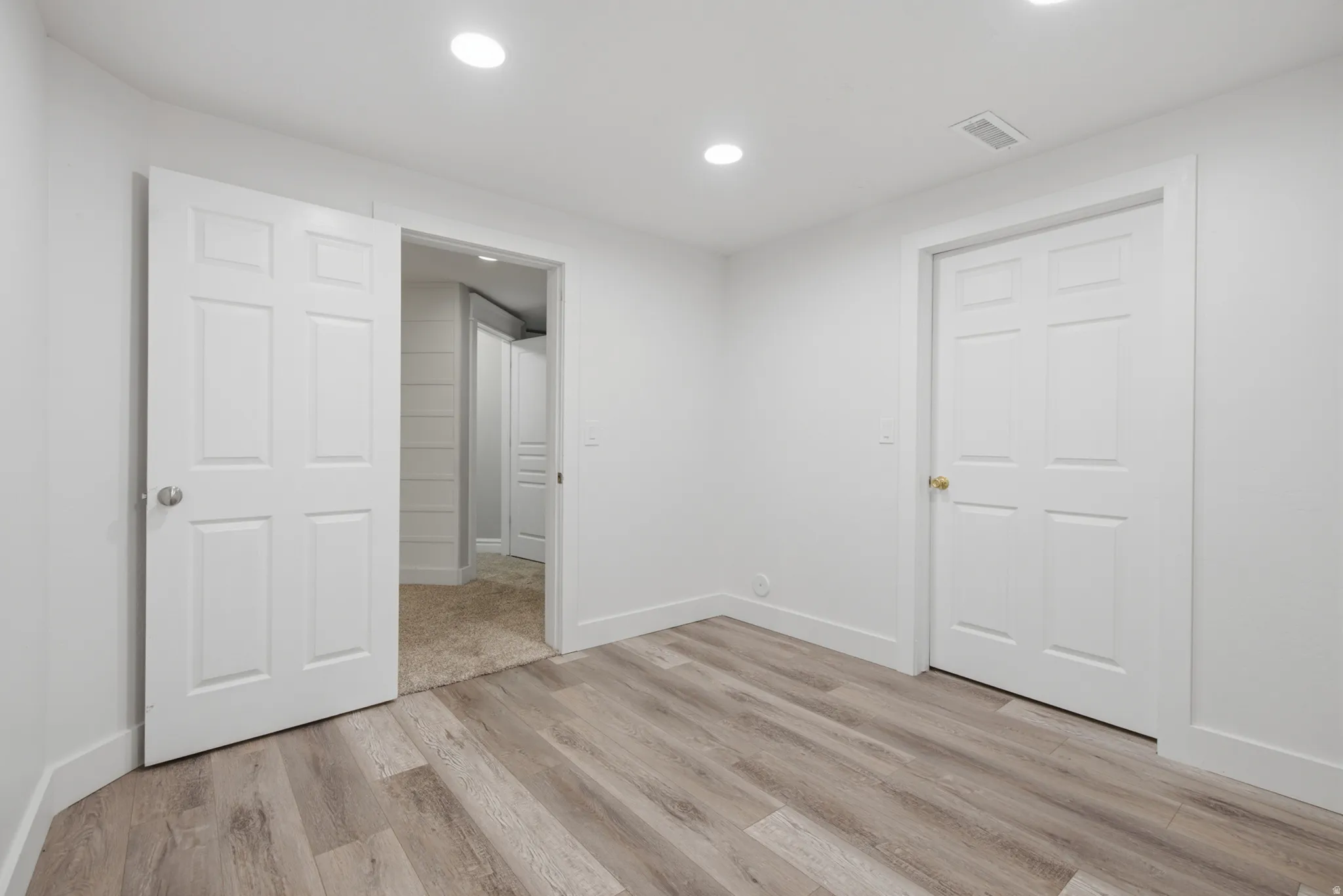 Recessed lighting, wood-finish flooring, white paneled doors, and crisp white walls