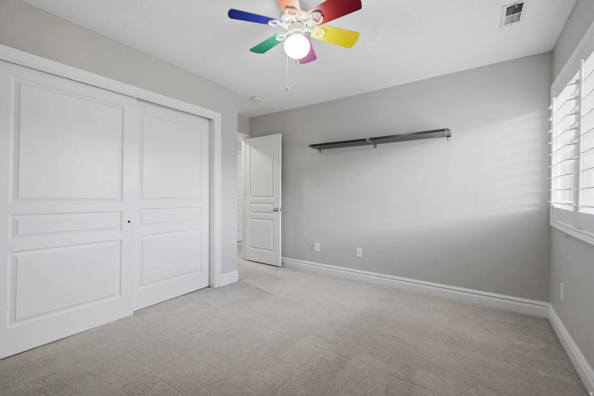 Plush carpeting, paneled closet doors, window with plantation shutters, and a ceiling fan with integrated lighting