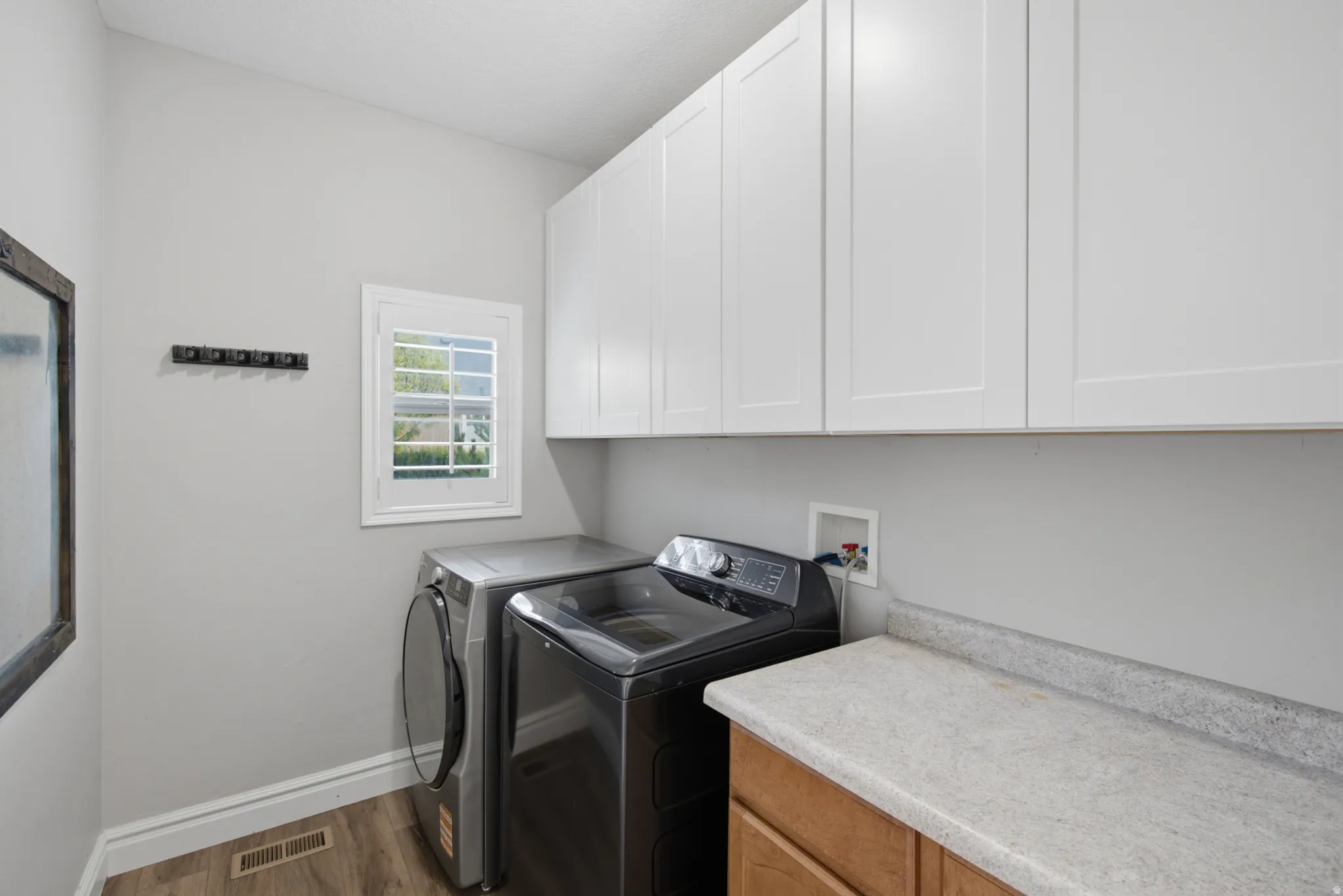 Upper white shaker-style cabinetry, wood-finish flooring, a single window, and a built-in countertop