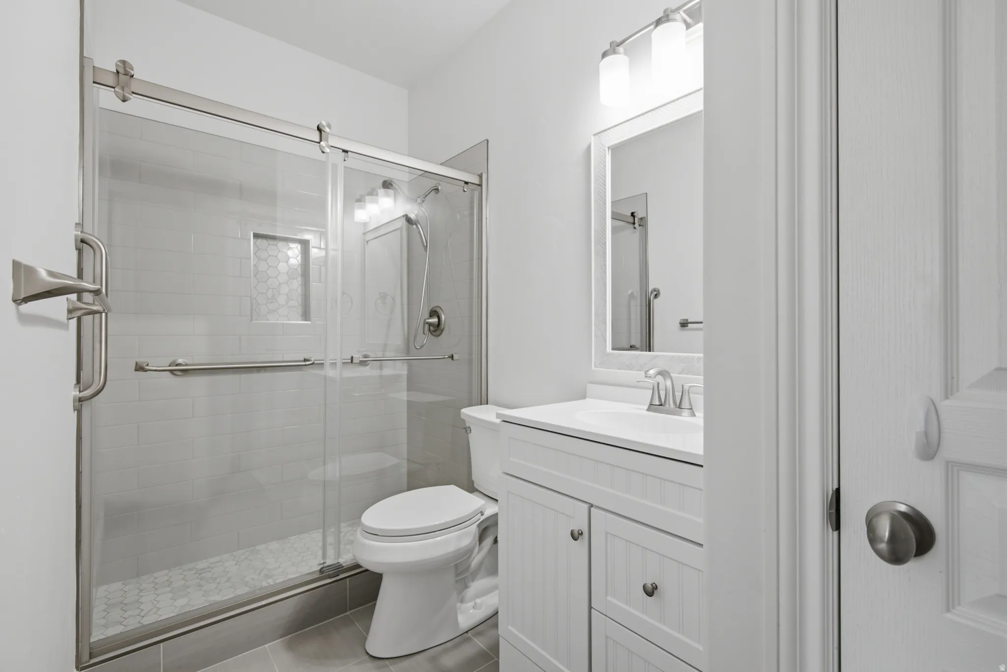 Fully tiled shower with sliding glass door, built-in shelving, and hexagonal floor tiles