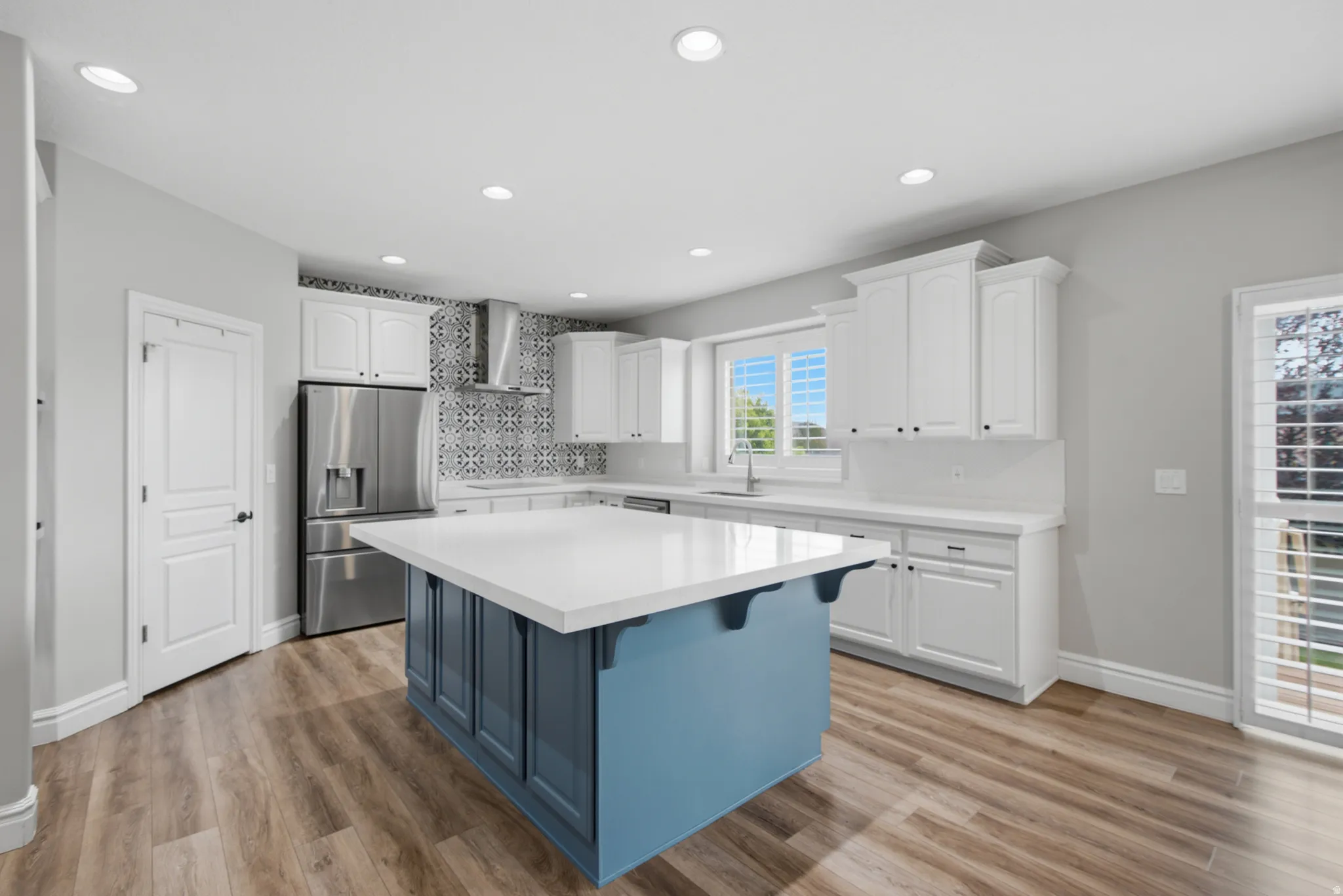 Kitchen featuring wood-finish flooring, recessed lighting, a blue island with a white countertop, white cabinetry, and a patterned tile backsplash
