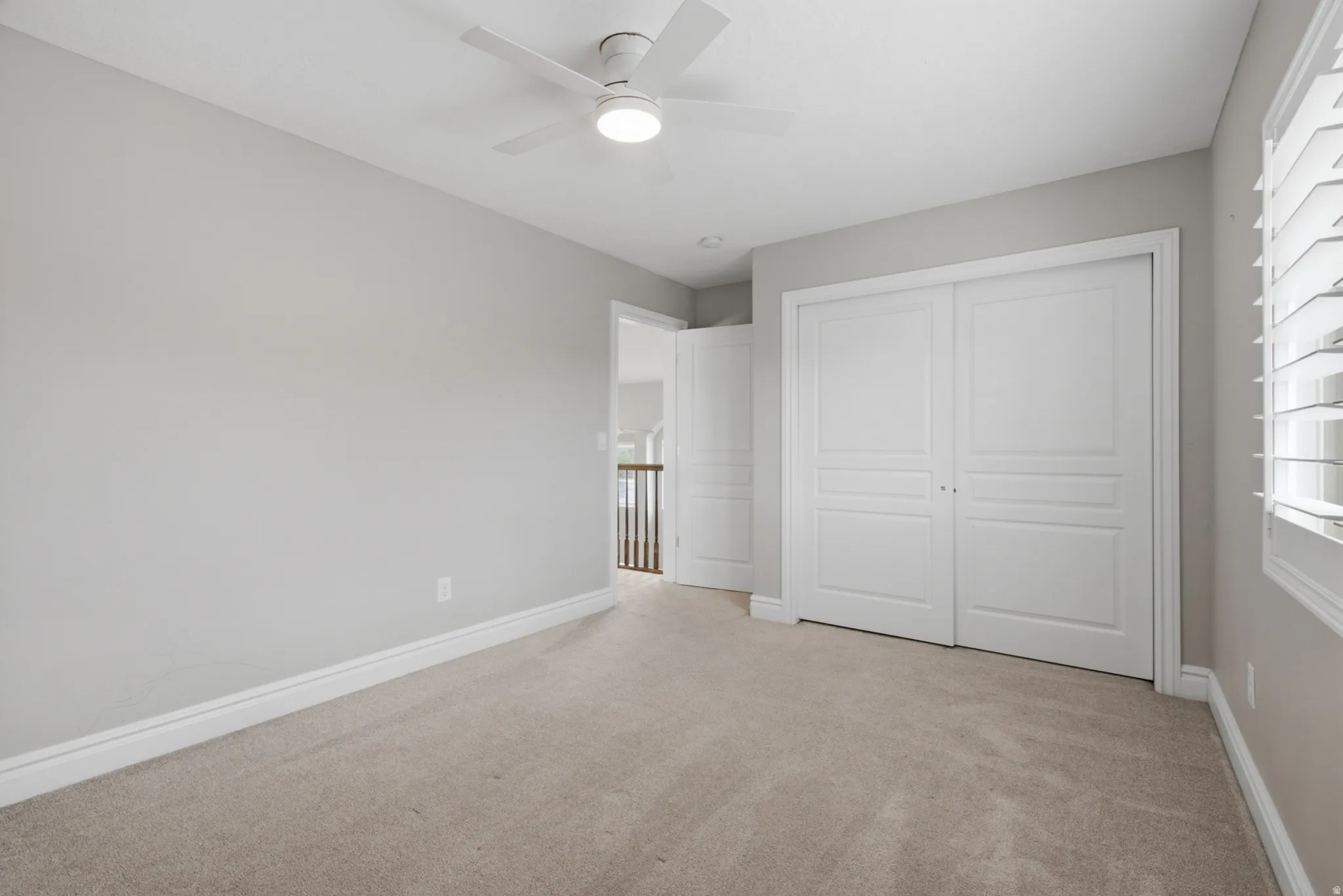 Plush carpeting, neutral wall tones, white bi-fold closet doors, ceiling fan with integrated lighting, and window with plantation shutters